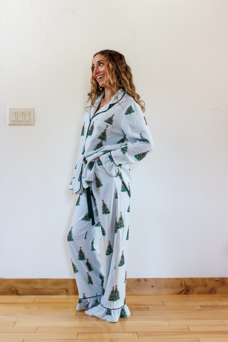 Woman wearing a light blue pajama set with tree pattern standing against a white wall.