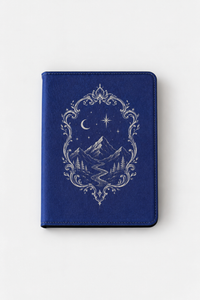 A blue notebook or journal with a silver-toned ornate border design featuring a mountain landscape, stars, and a crescent moon on the front cover, shown against a plain light background.