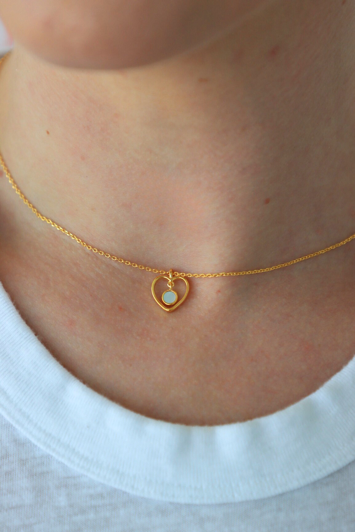 Gold necklace with a heart-shaped pendant worn by a person