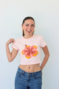 Woman wearing a pink crop top with a floral design and blue jeans against a light gray background