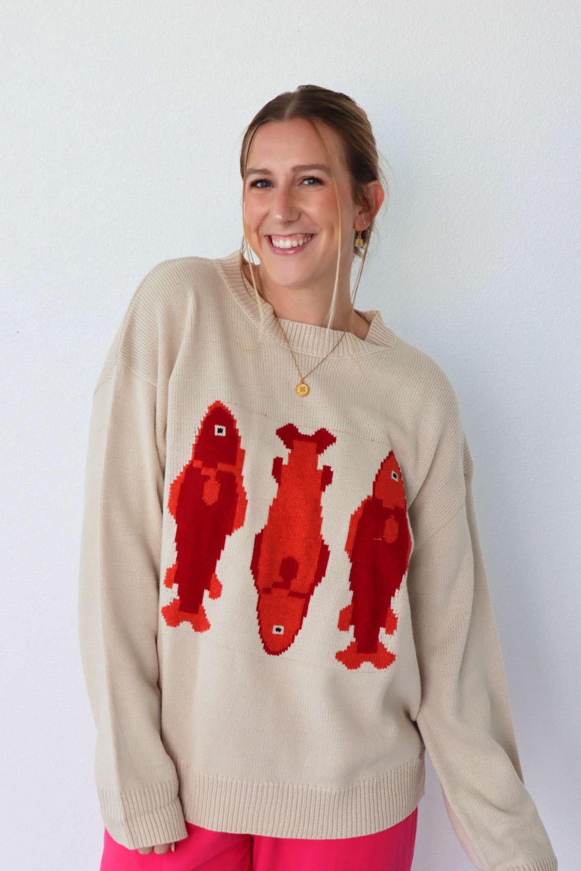 Woman wearing a beige sweater with red fish patterns against a white background