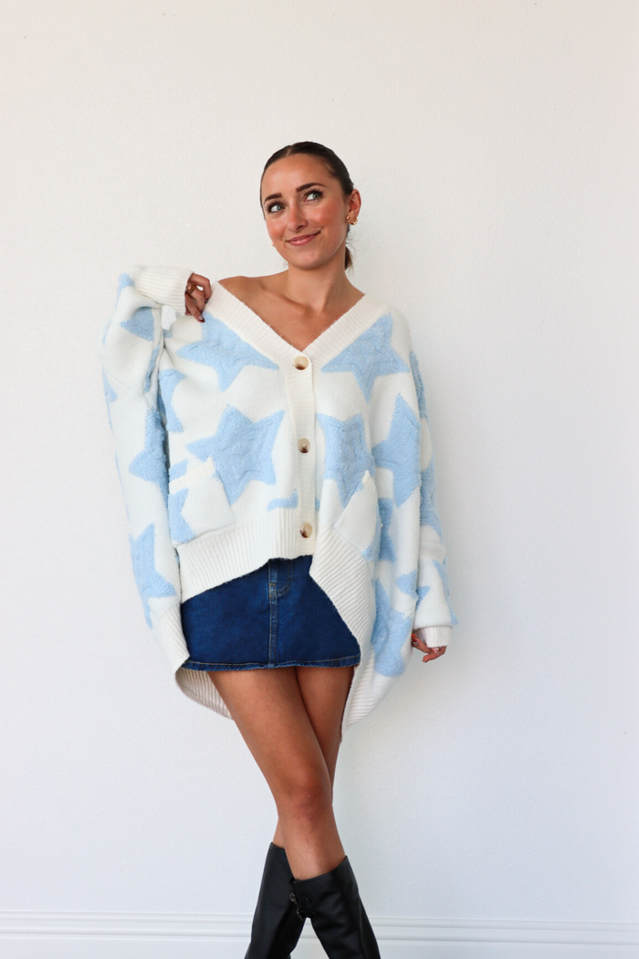 Woman wearing a blue and white patterned cardigan over a white shirt with a denim skirt and black knee-high boots.