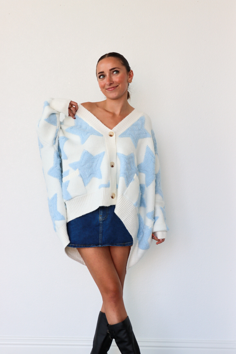 Woman wearing a blue and white patterned cardigan over a white shirt with a denim skirt and black knee-high boots.