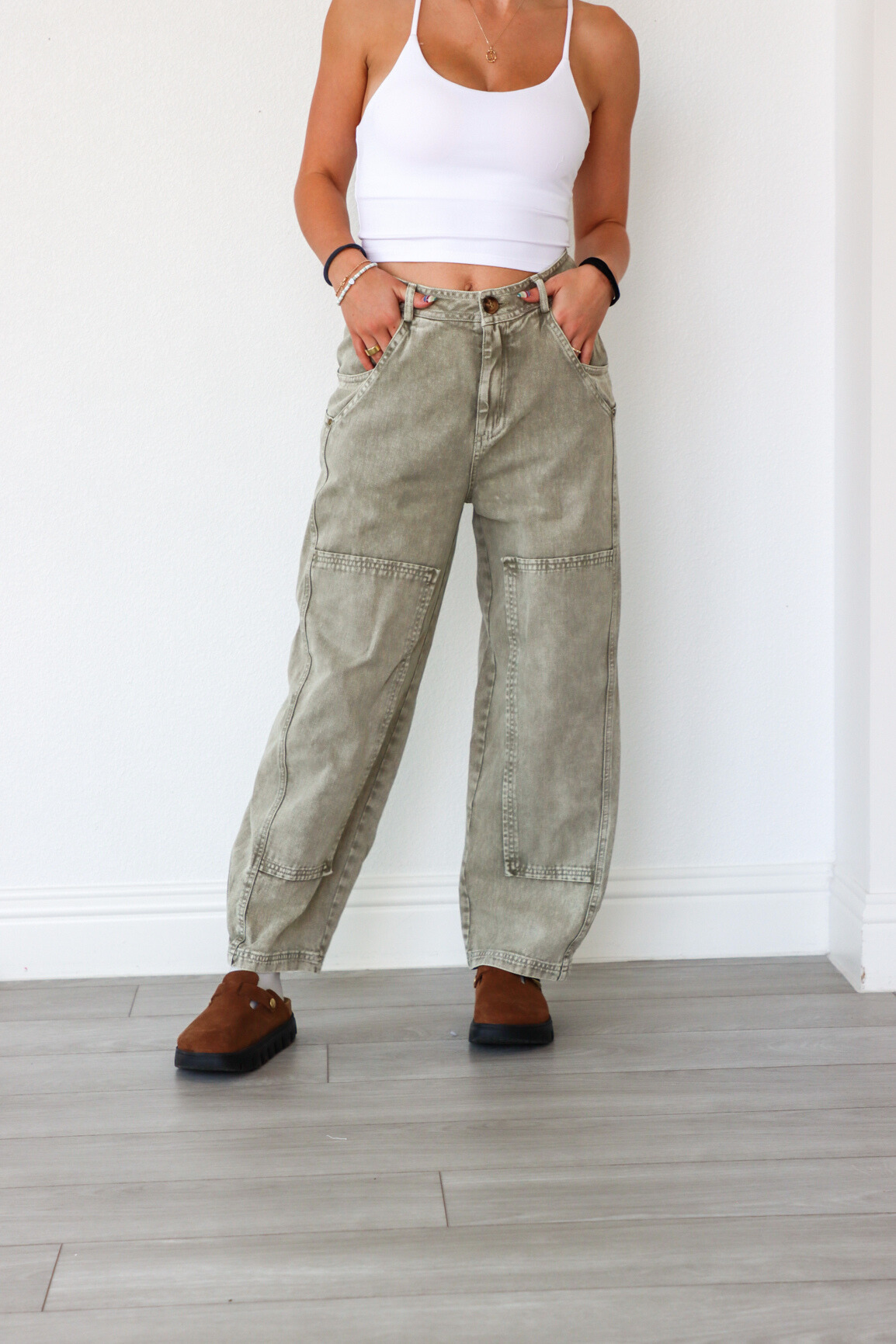 Person wearing light-colored cargo pants and a white tank top against a white wall.