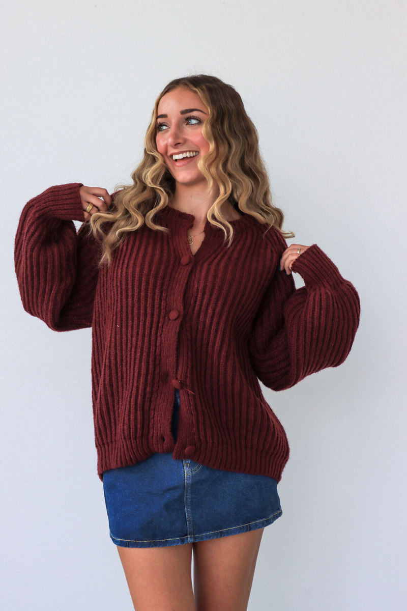 Woman wearing a maroon ribbed sweater and blue skirt against a white background