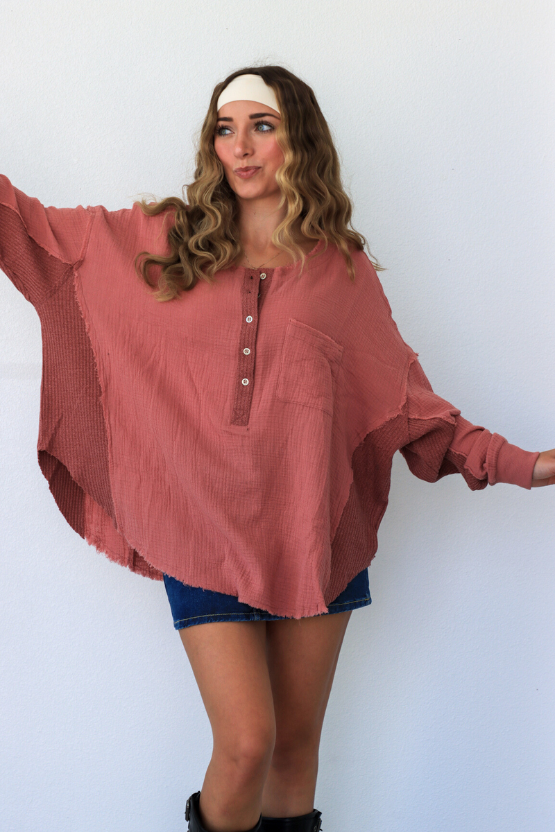 Woman wearing a pink oversized shirt and denim shorts against a white background