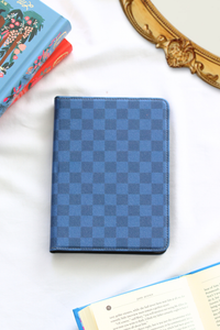 Blue checkered notebook on a white surface with books and a decorative object in the background