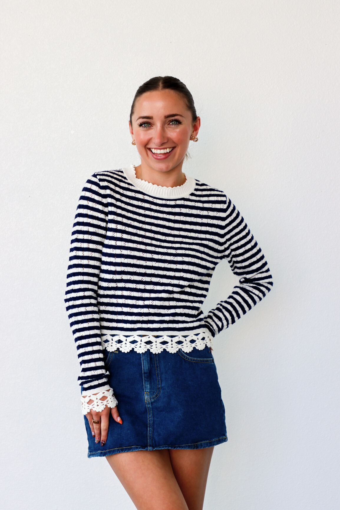 Woman wearing a black and white striped sweater with lace trim and a denim skirt on a white background