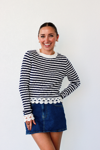 Woman wearing a black and white striped sweater with lace trim and a denim skirt on a white background