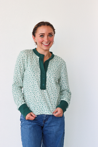 Woman wearing a green and white patterned shirt with blue jeans against a white background