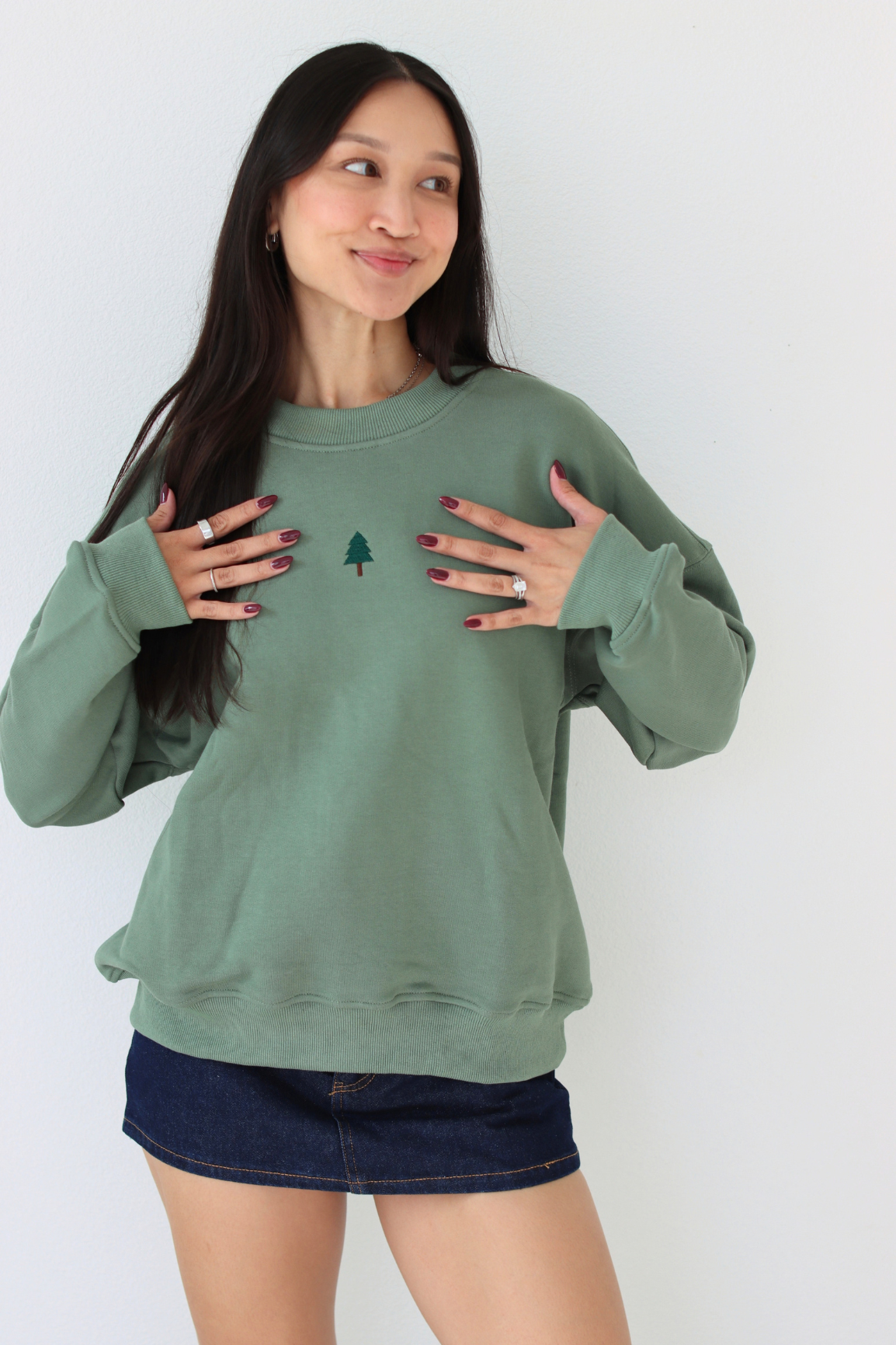 Woman wearing a green crewneck sweater with a embroidered tree in the center