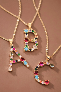 Three gold necklaces with letter pendants 'A', 'B', and 'C' on a brown background