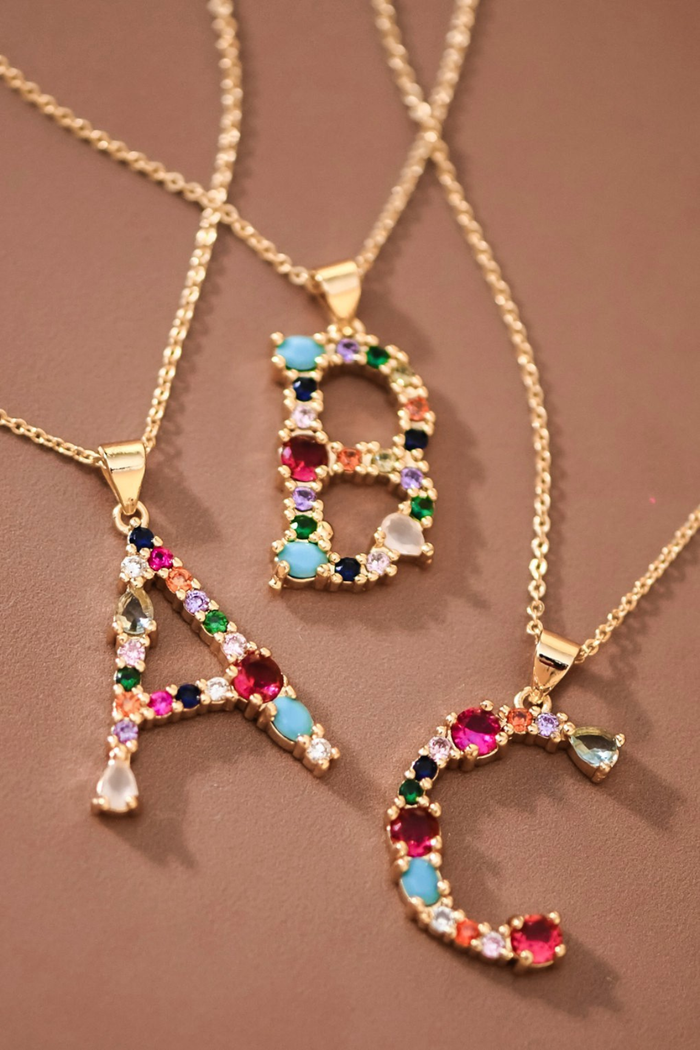 Three gold necklaces with letter pendants 'A', 'B', and 'C' on a brown background