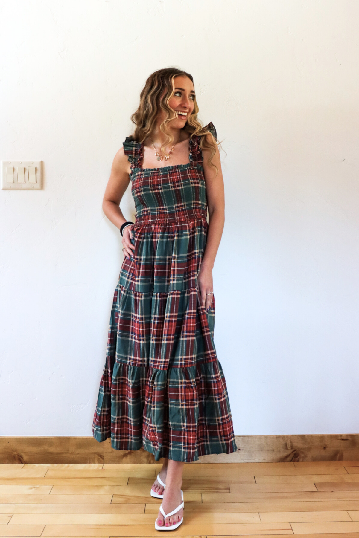Woman wearing a plaid dress standing against a white wall.