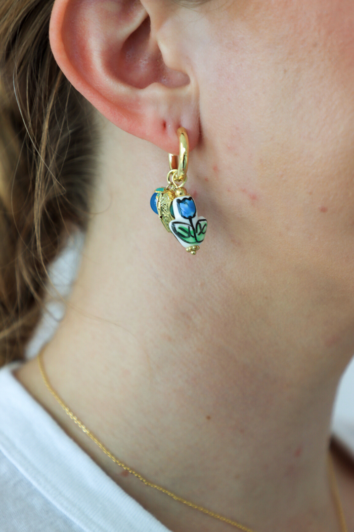 Close-up of a gold earring with colorful details worn by a person.