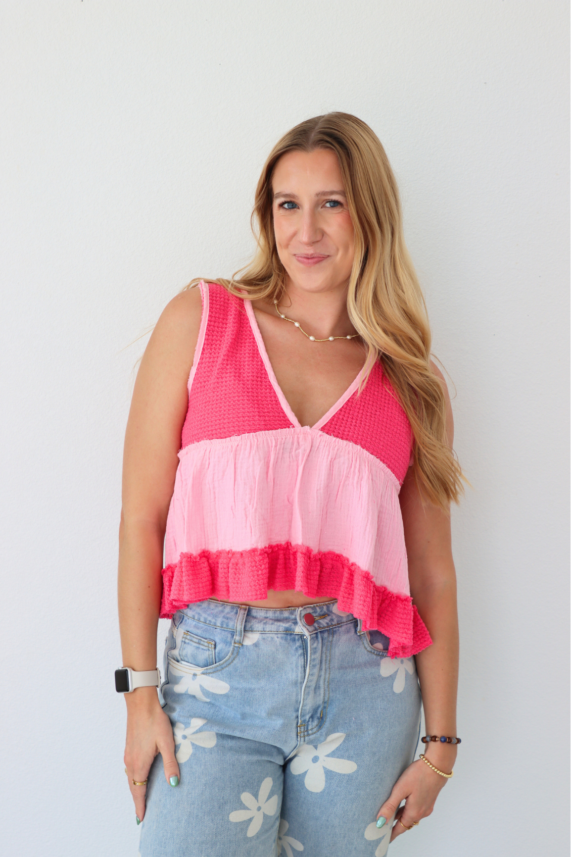 Woman wearing a pink and white top with floral jeans against a plain background