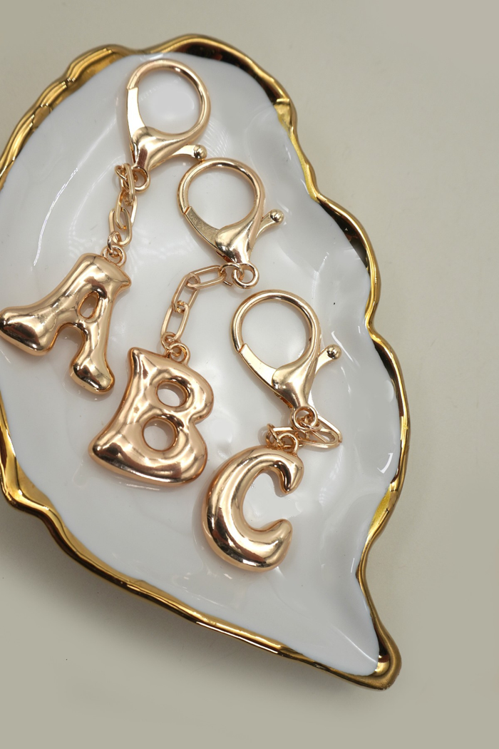 Gold letter charms 'A', 'B', and 'C' on a white dish with gold rim.