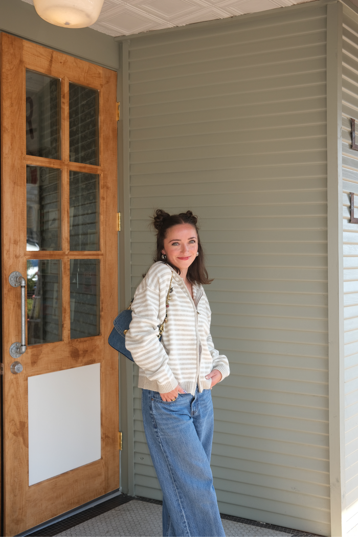 Woman wearing a tan and white striped zip-up sweater with blue denim jeans 