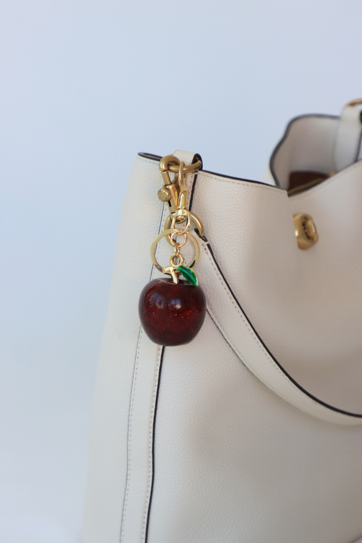 White handbag with a cherry charm on a light blue background