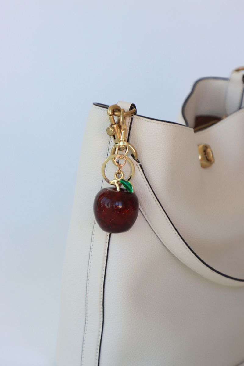 White handbag with a cherry charm on a light blue background