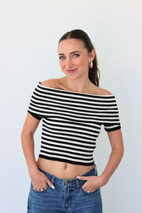 Woman wearing a black and white striped off-shoulder top and blue jeans against a plain background