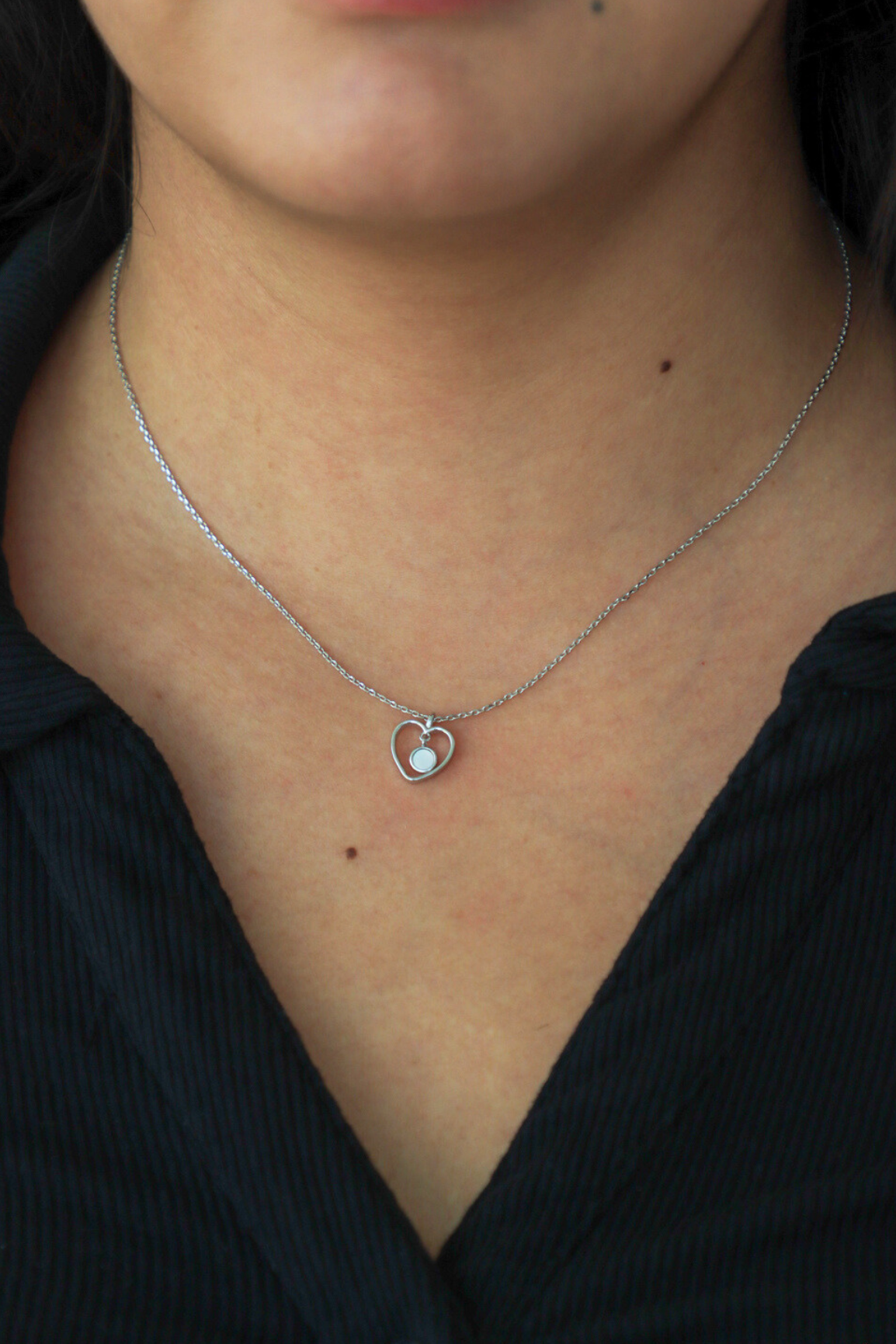 Necklace with a heart-shaped pendant worn by a person against a black background