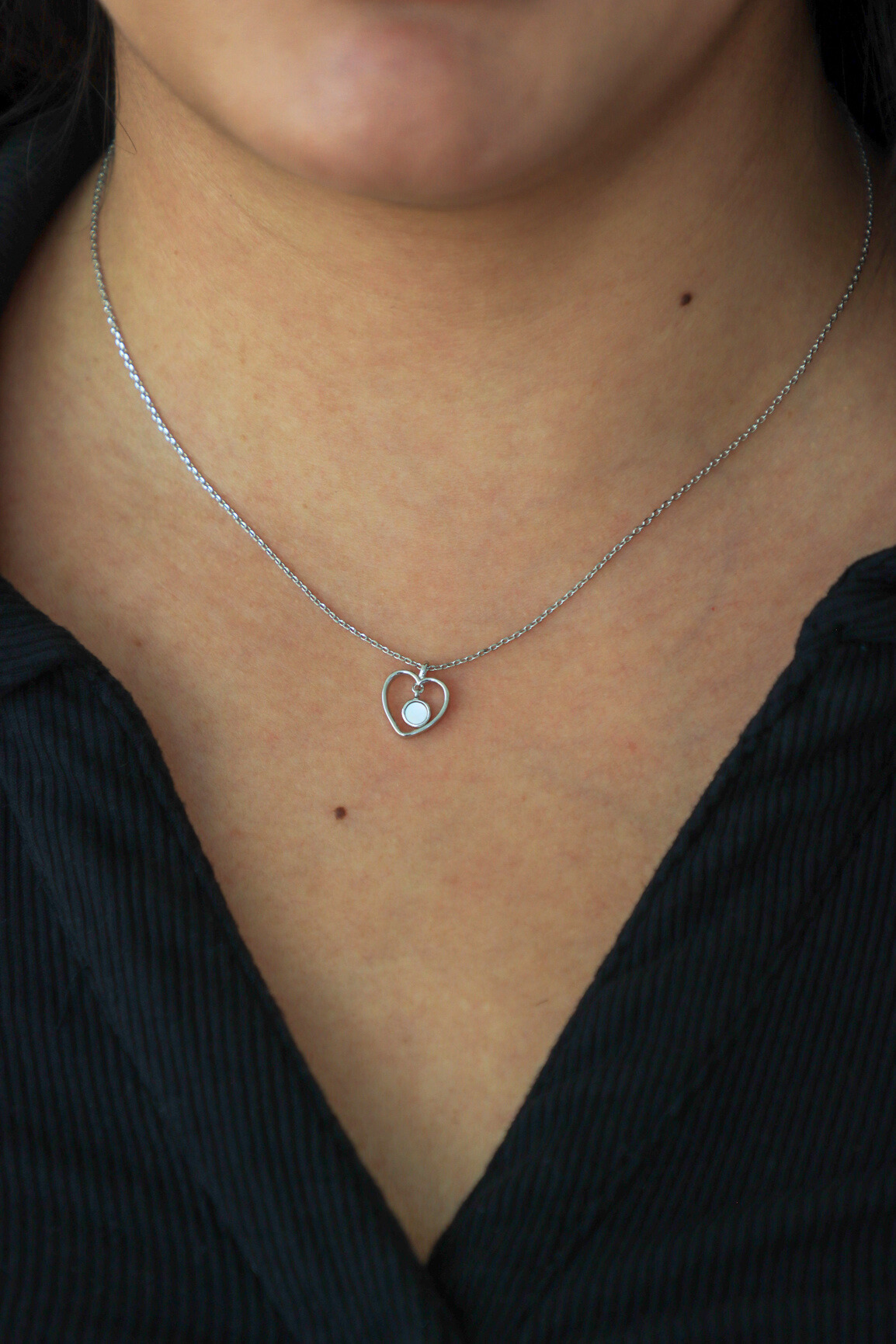 Silver necklace with a heart-shaped pendant worn by a person against a black background