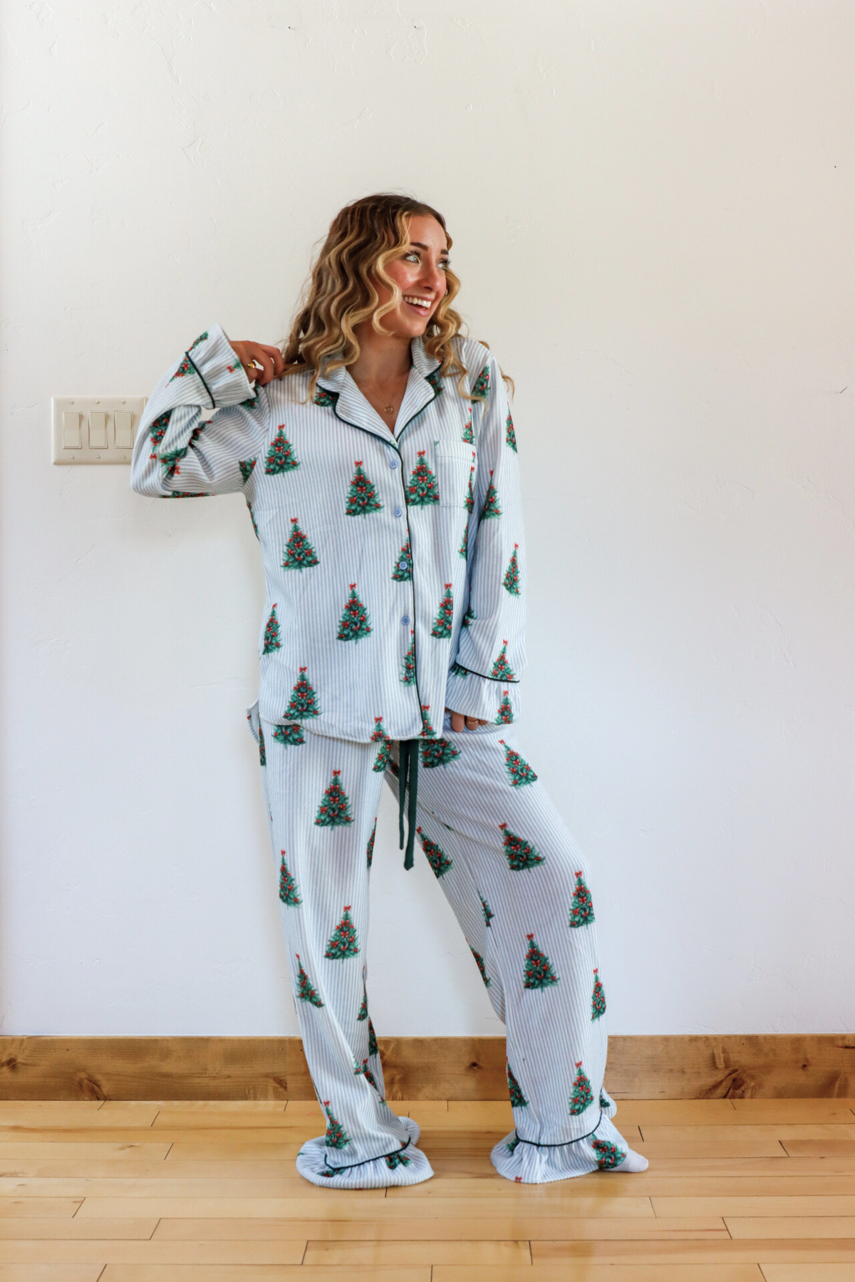 Woman wearing a festive pajama set with Christmas tree pattern in a room.