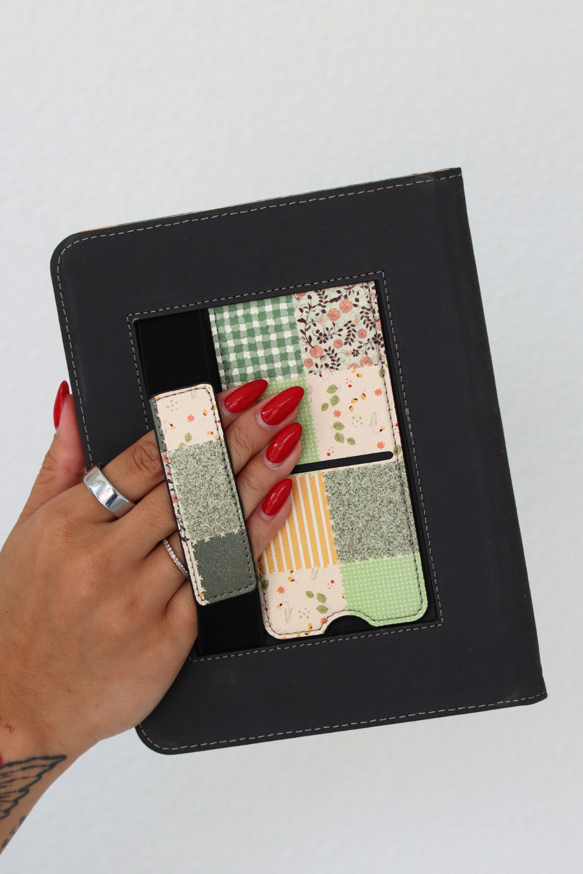 A hand with red manicured nails holds a nook case with a kickstand and hand strap.