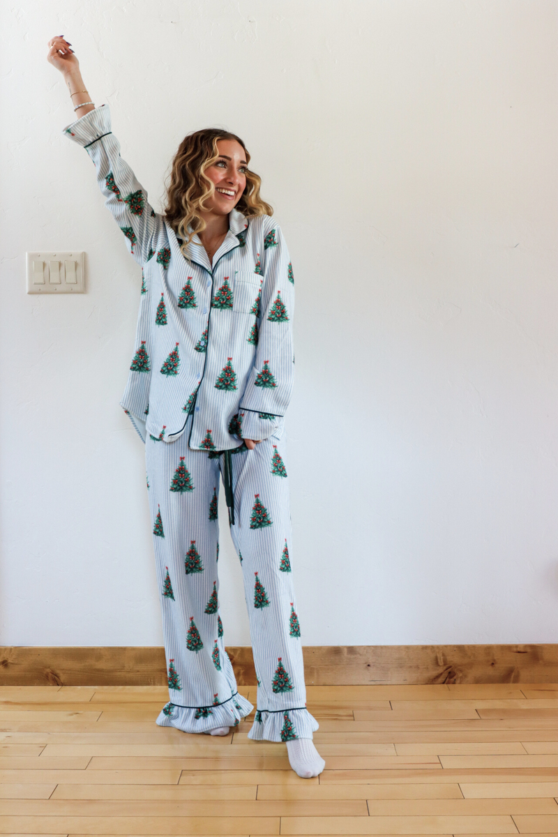 Woman wearing a festive pajama set with Christmas tree pattern in a room.