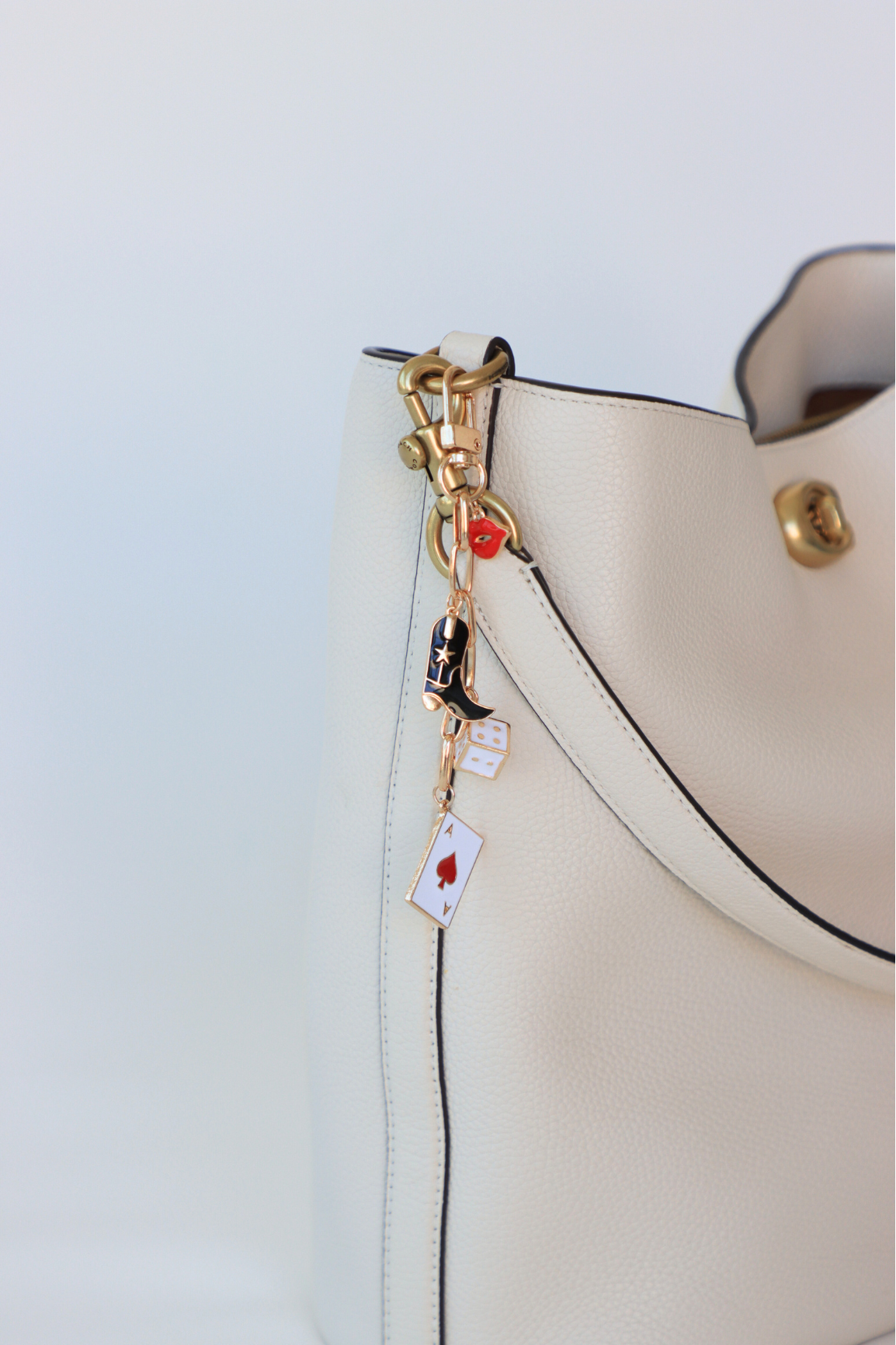 Close-up of a beige handbag with decorative charms on a light blue background