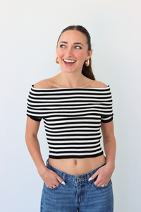 Woman wearing a black and white striped off-shoulder top and blue jeans against a plain background