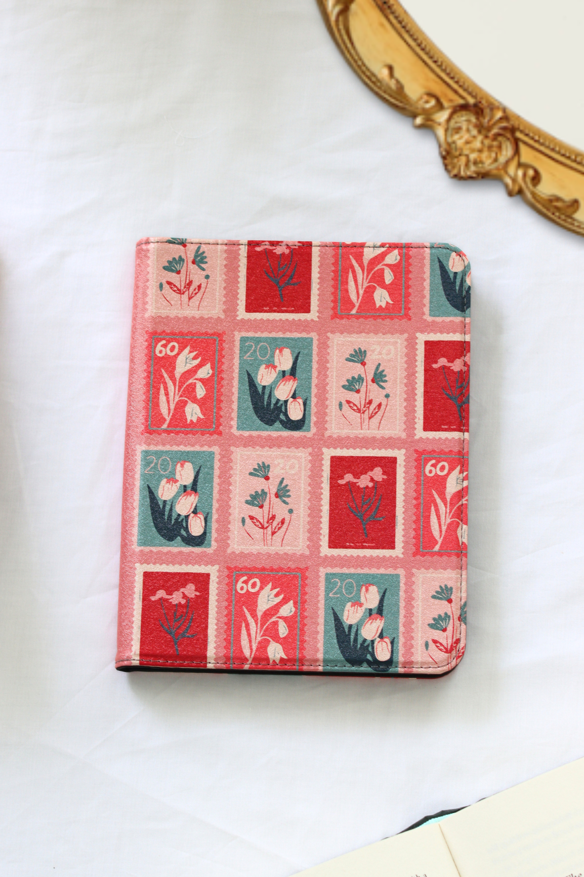 A nook case featuring a vintage-style postage stamp pattern with red, pink, and teal floral designs, photographed on a light fabric background.