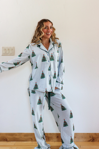 Woman wearing Christmas tree-patterned pajamas standing against a white wall.