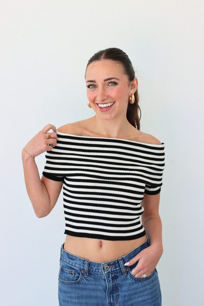 Woman wearing a black and white striped off-shoulder top and blue jeans against a plain background