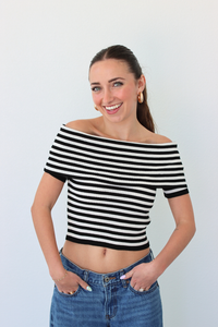 Woman wearing a black and white striped off-shoulder top and blue jeans against a plain background