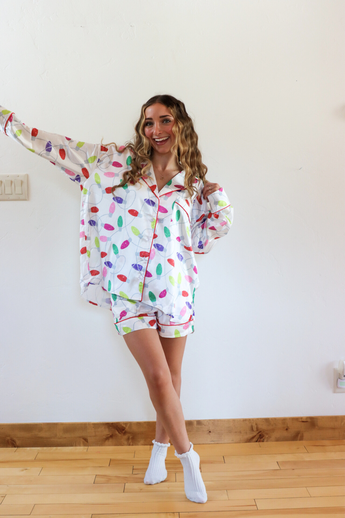 Woman wearing a colorful pajama set in a room with wooden flooring and a white wall.