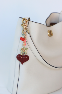 Decorative charm with a heart and star on a white handbag against a light blue background
