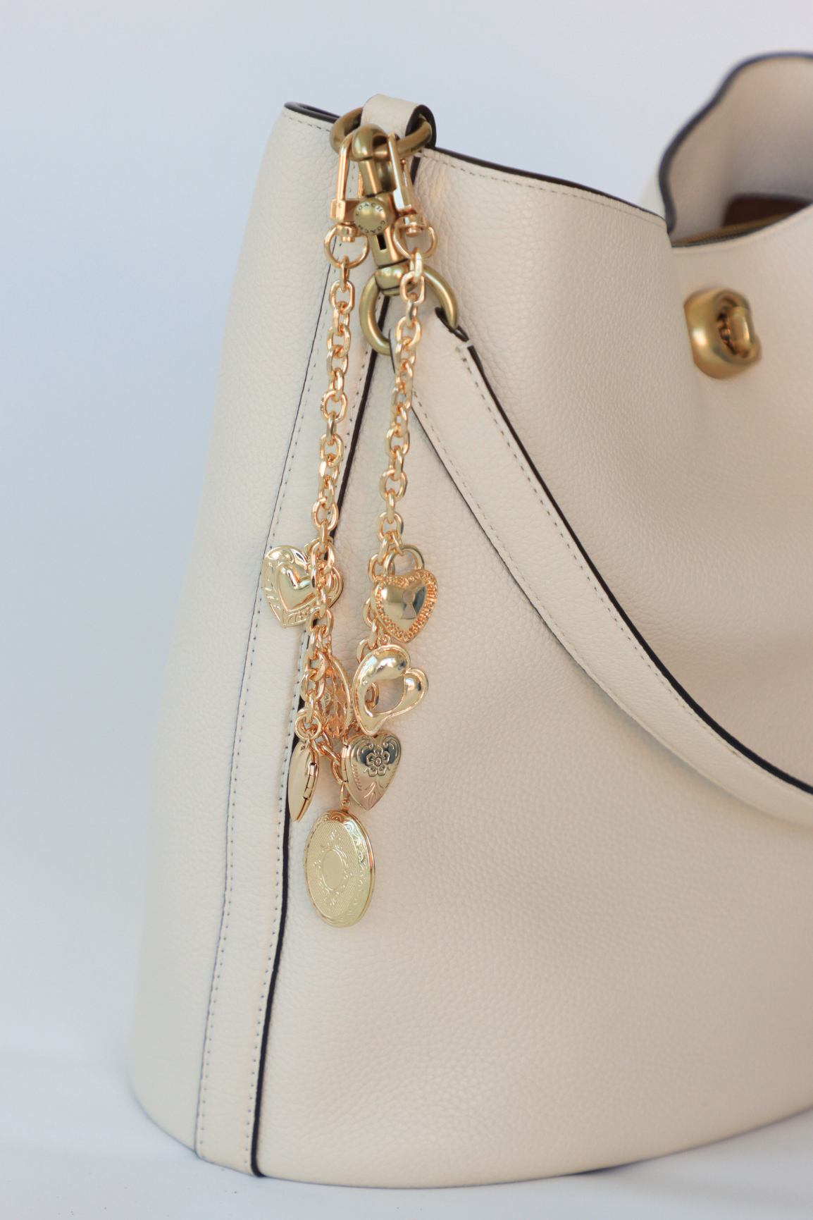 White handbag with gold chain and heart-shaped charms on a light gray background