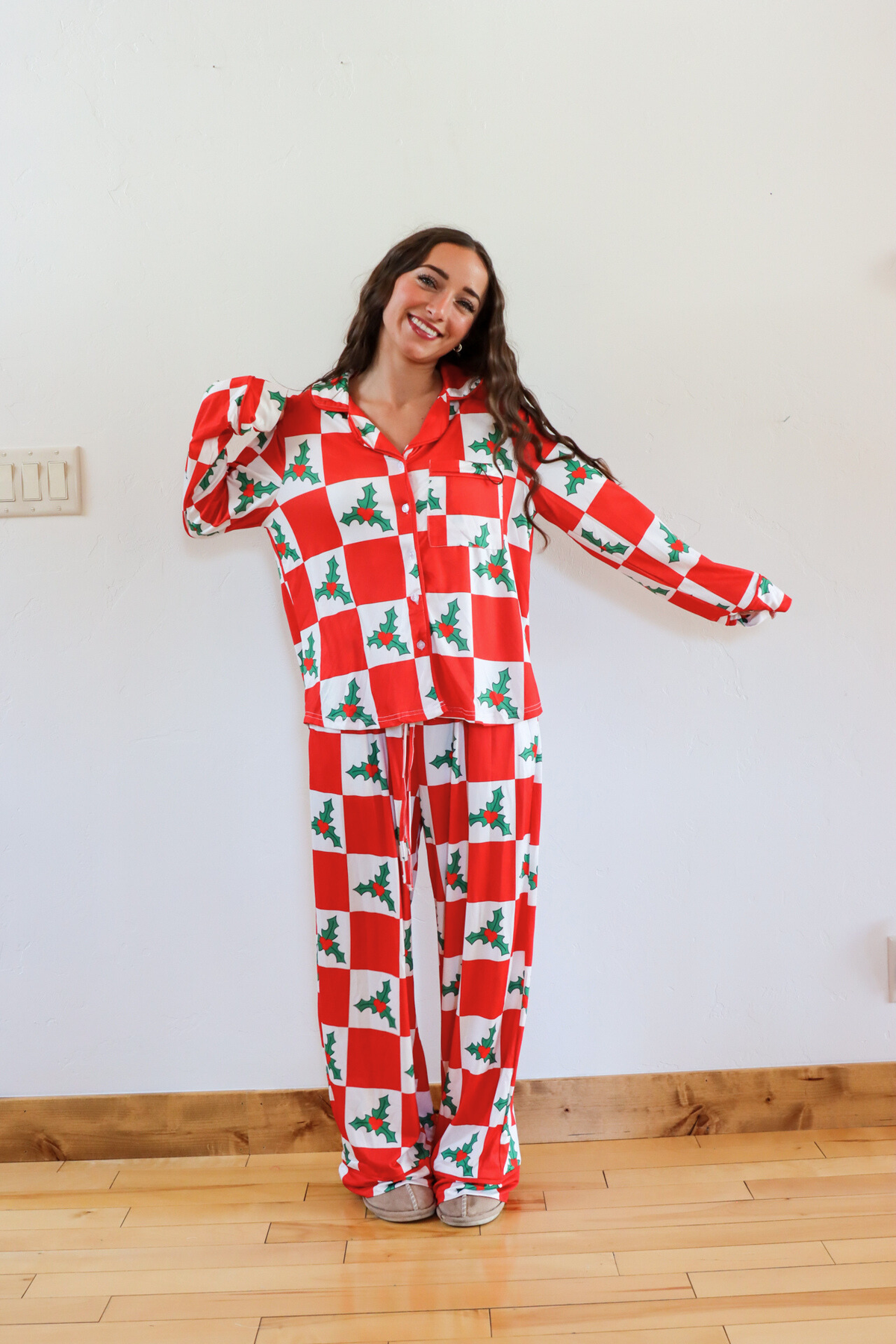 Person wearing a red and white checkered pajama set with holly design on a wooden floor.