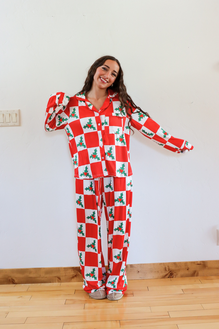 Person wearing a red and white checkered pajama set with holly design on a wooden floor.