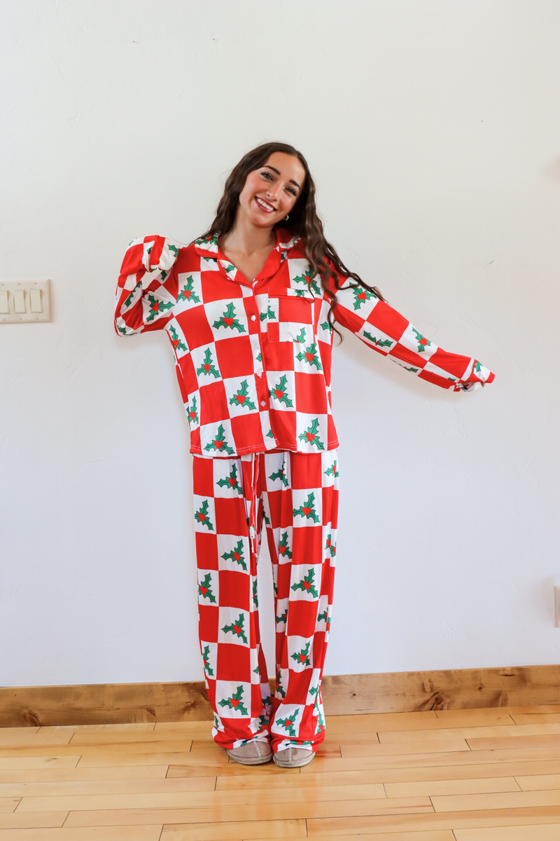 Person wearing a red and white checkered pajama set with holly design on a wooden floor.