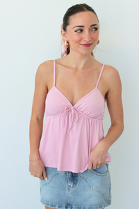 Woman wearing a pink spaghetti strap top and denim skirt against a light background