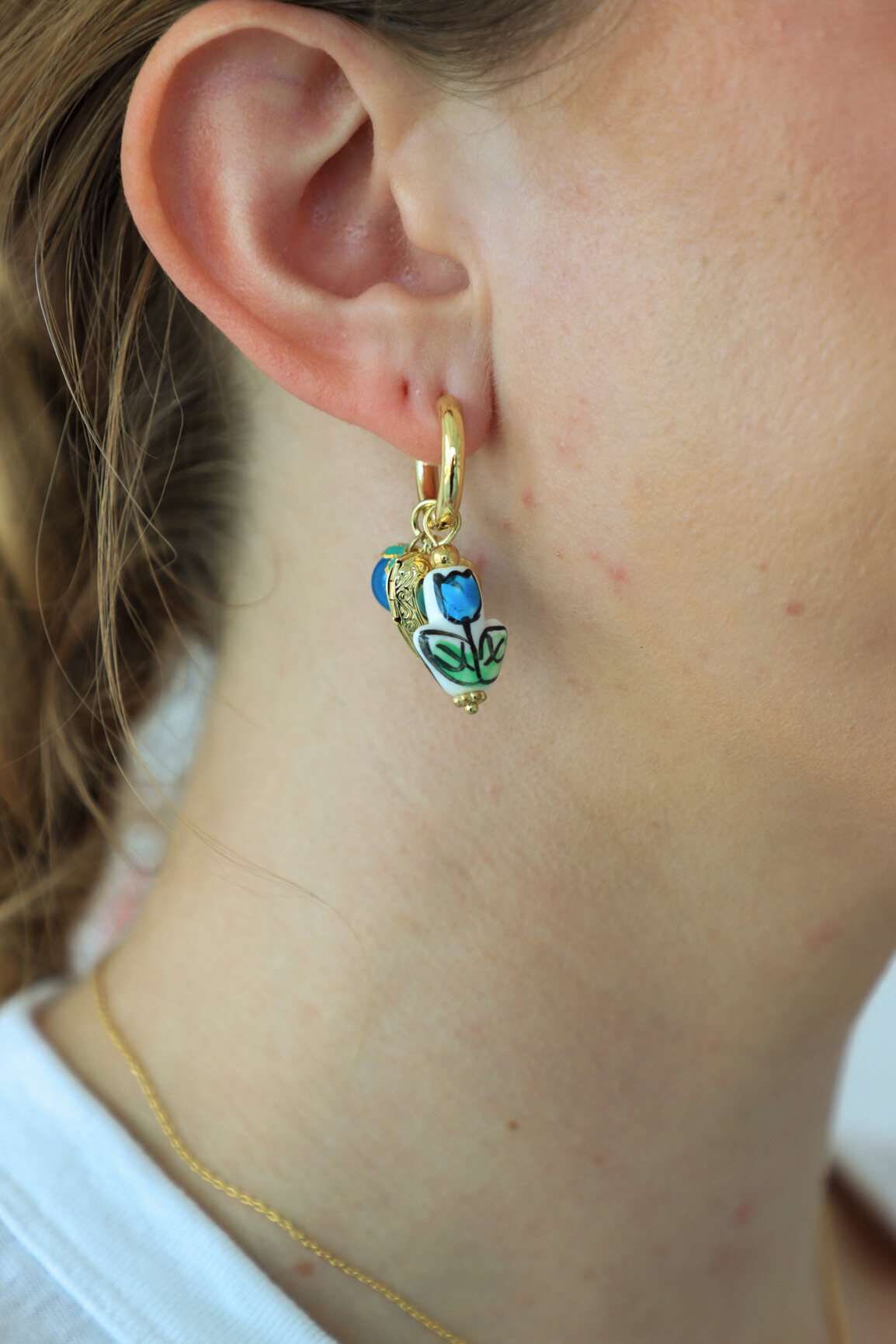 Close-up of a gold earring with a blue gemstone worn by a person.