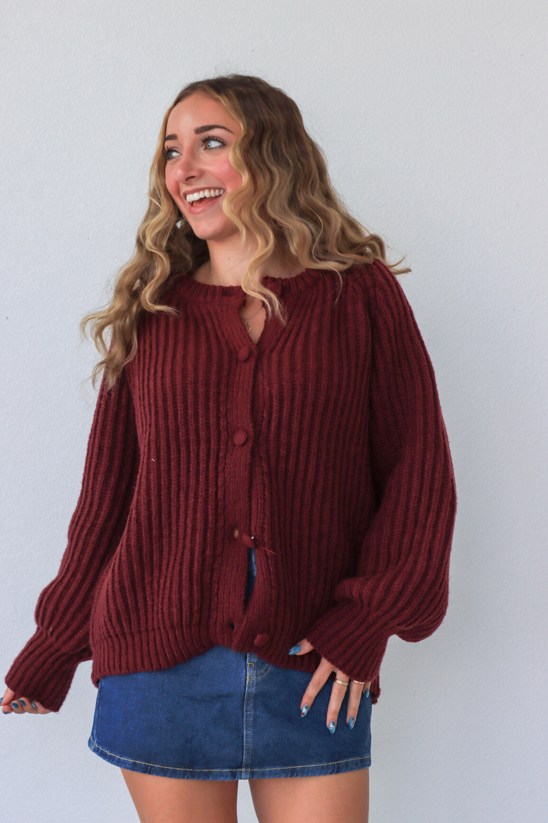 Woman wearing a burgundy sweater and denim skirt against a white background