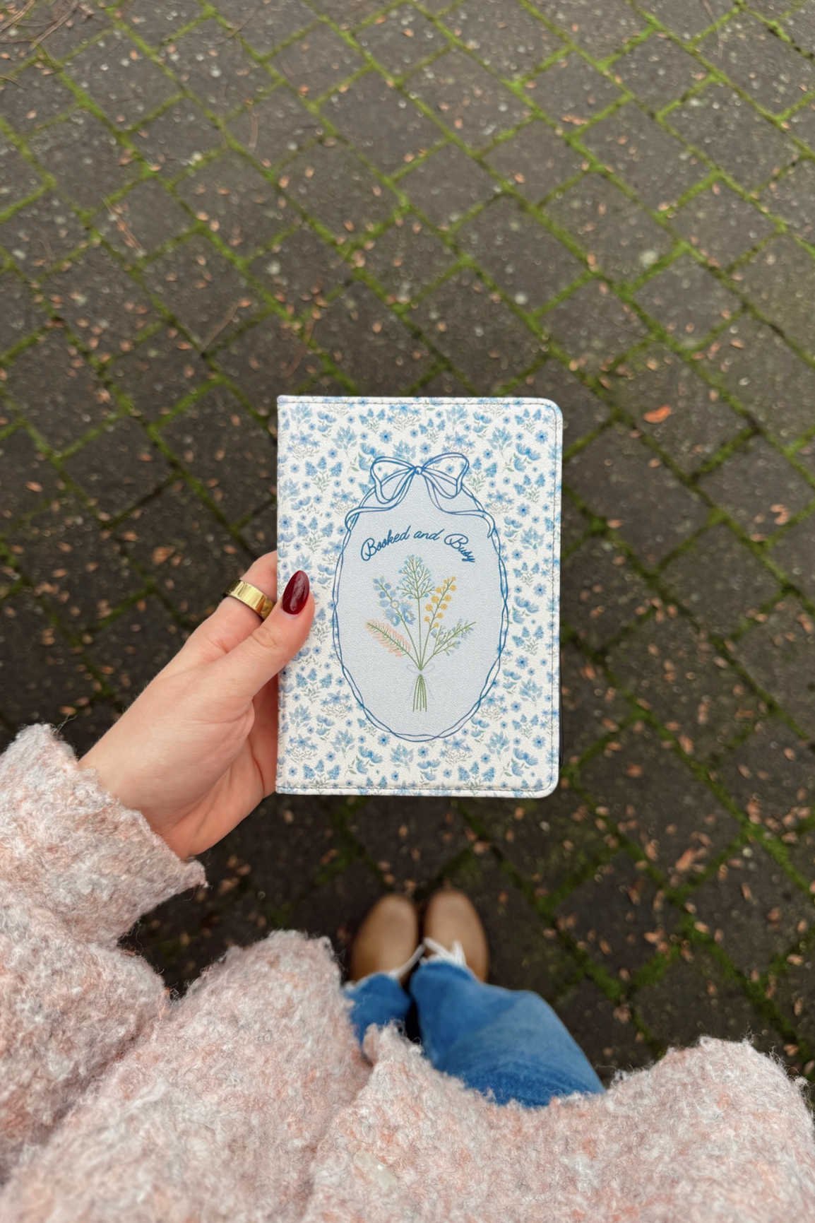 Hand holding a small floral notebook on a textured pavement background