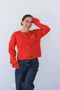 Person wearing a red cardigan with text and blue jeans against a white background