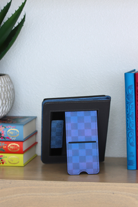Black and blue checkered wallet on a wooden surface with books and a plant in the background
