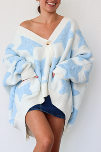 Person wearing a white and blue patterned cardigan over a denim skirt on a white background