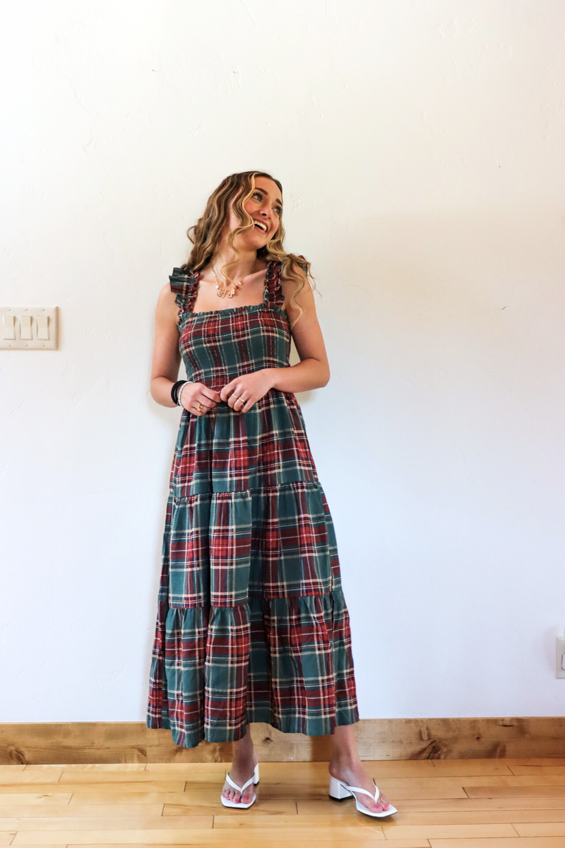 Woman wearing a plaid dress standing against a white wall.